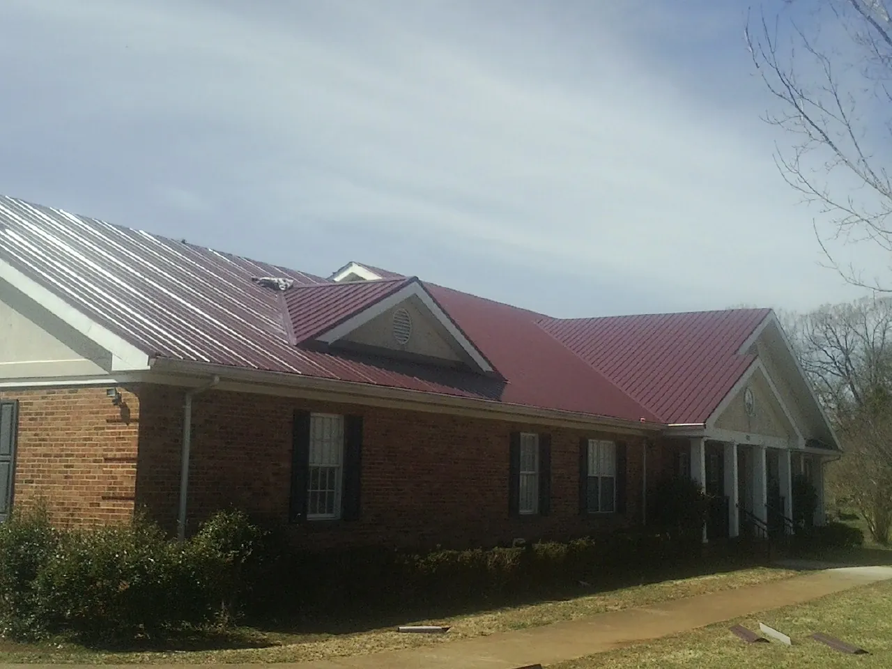 Red metal roof with gabled entries on a long brick building, from a Hail Damage Roof Repair job in Summitville