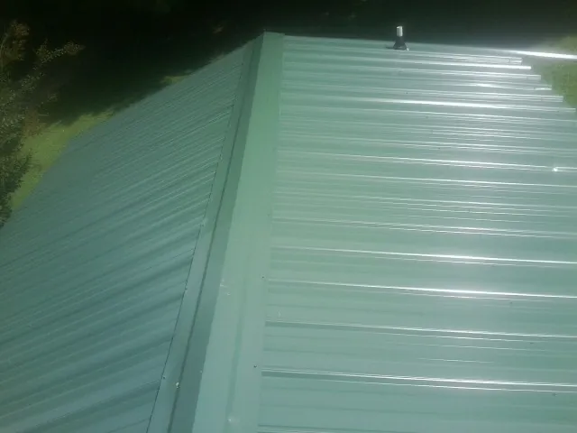 New green metal panels meeting at the ridge of a roof — Flat Roof Repair work by our crew in Summitville