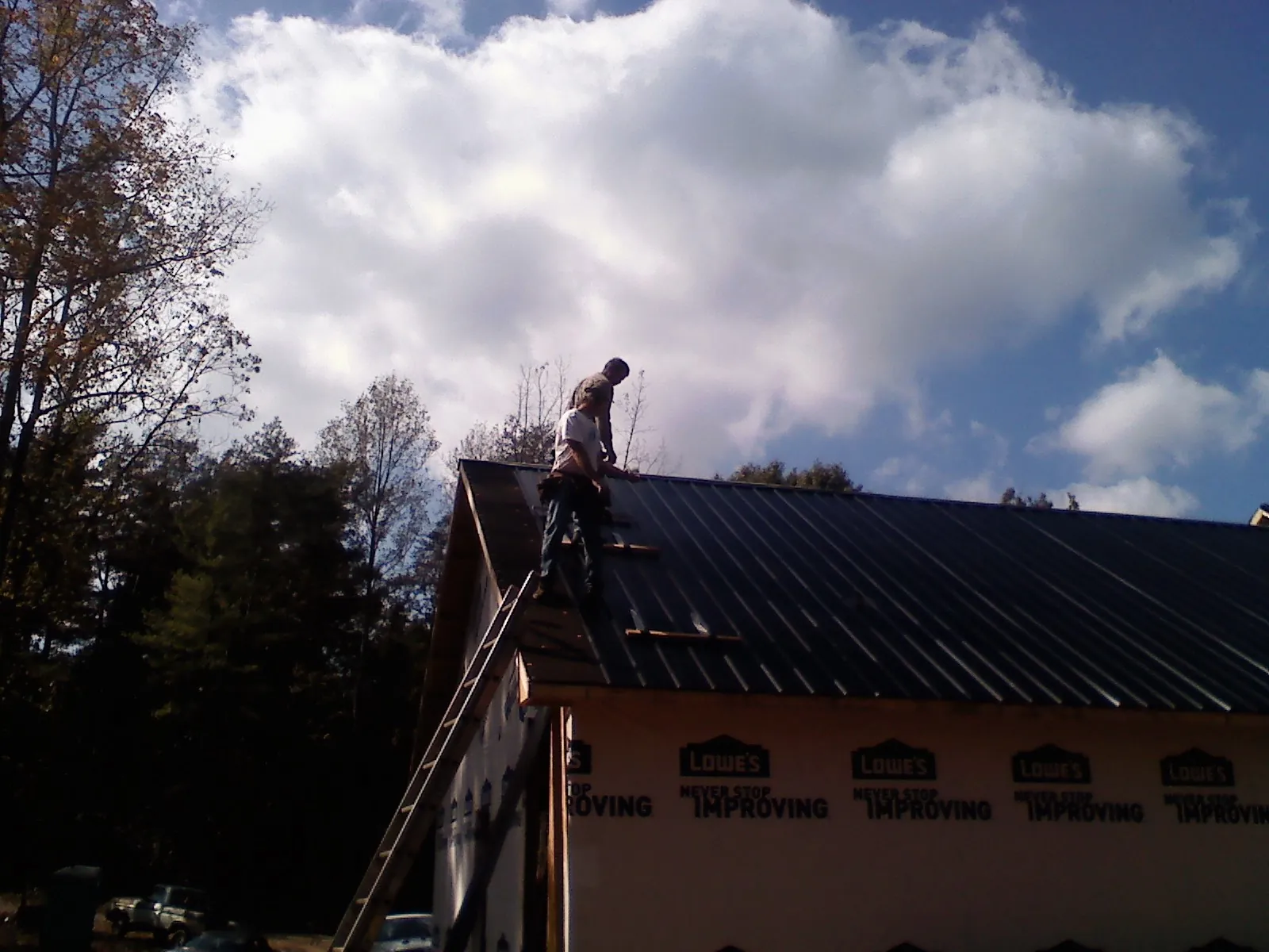 Roofer fastening dark metal panels high against a cloudy sky, from a Roof Inspection job in Summitville