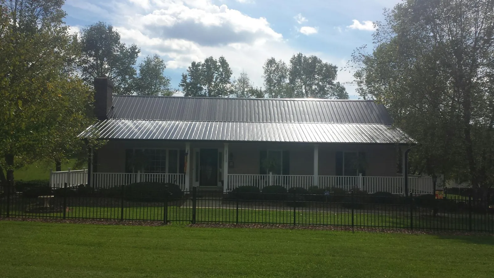 Gray metal roof on a brick ranch with a full width front porch — Gutter Guard Installation work by our crew in Summitville